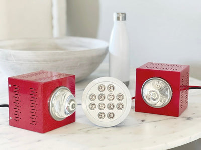 Three red light therapy devices and a wooden bowl and a water bottle sitting on a white marble table.
