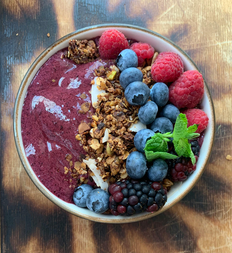 Acai Berry smoothie bowl with granola and fresh Acai berries on a wooden surface
