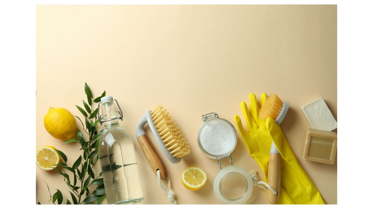 Cleaning supplies including a lemon, bottle, scrub brush, gloves, and sponge on a beige background